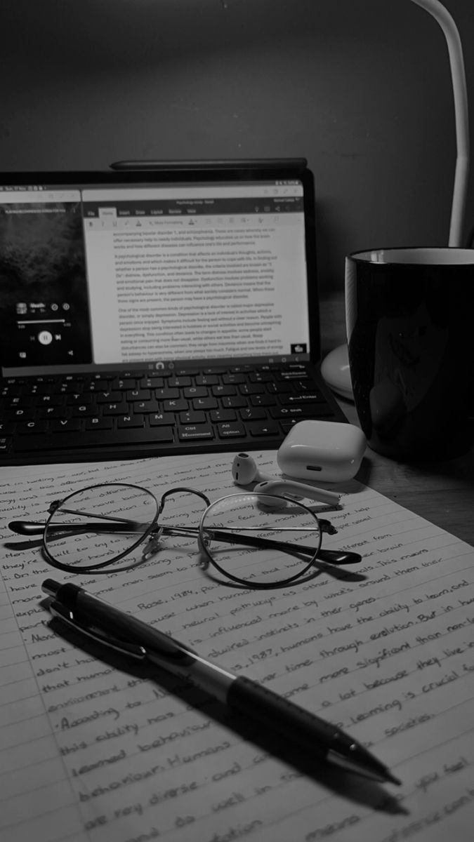 Handwritten notes, glasses and a pen beside a laptop on a writing desk
